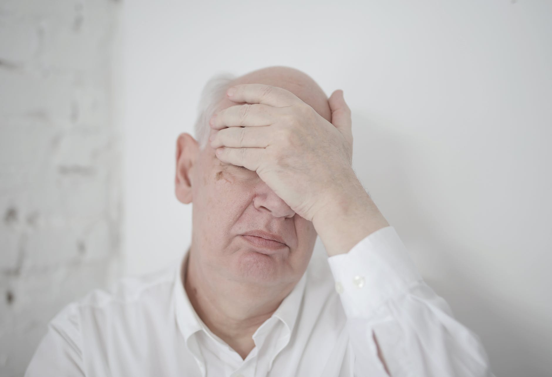 senior man covering face with hand while sitting near wall